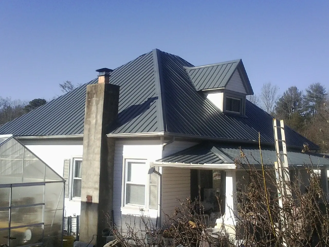 Dark blue standing seam metal roof on a white farmhouse with dormer — Slate & Tile Roof Repair by Roofing Brothers in Farmersburg