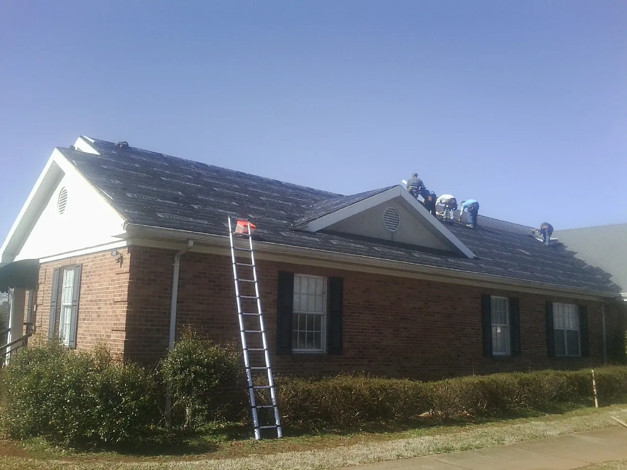 Crew tearing shingles off a brick ranch roof with a ladder set — Metal Roof Repair work by our crew in Farmersburg