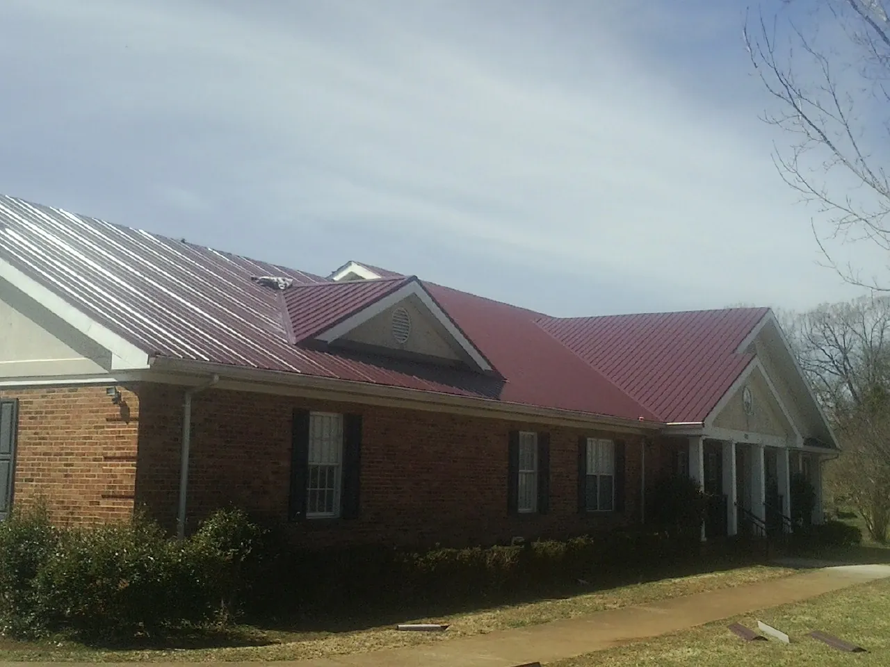 Red metal roof with gabled entries on a long brick building, from a Hail Damage Roof Repair job in Farmersburg