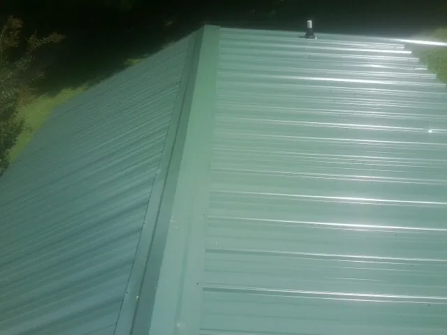 New green metal panels meeting at the ridge of a roof — Flat Roof Repair work by our crew in Farmersburg