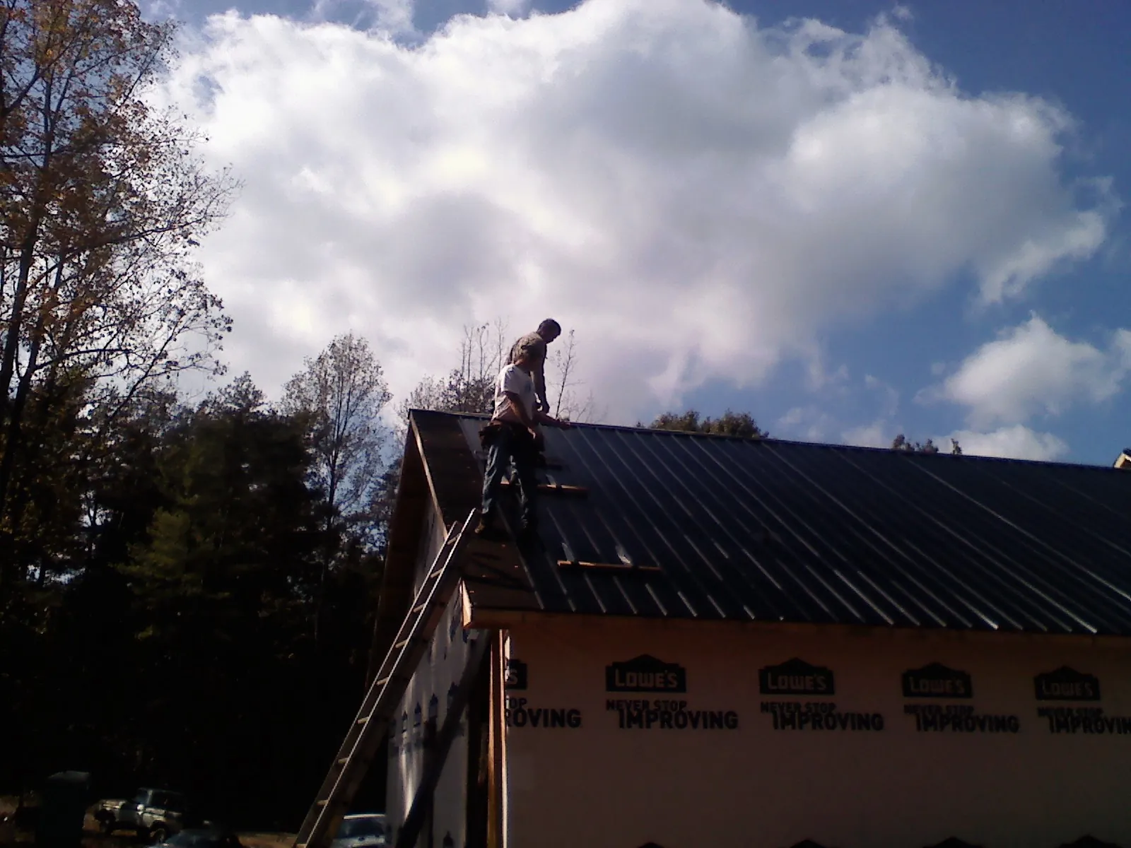 Roofer fastening dark metal panels high against a cloudy sky, from a Roof Inspection job in Farmersburg