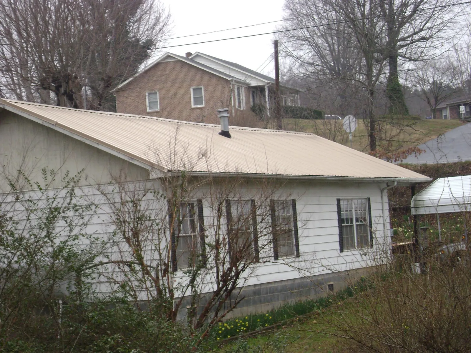 Tan metal roof on a white sided house set into a hillside — Commercial Roofing by Roofing Brothers in Farmersburg